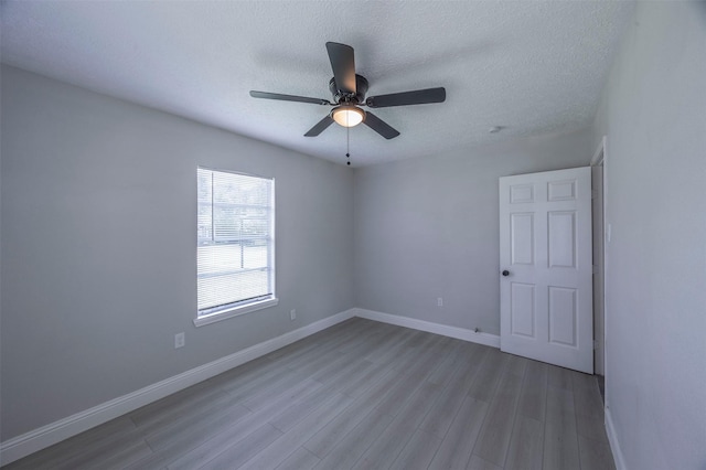 spare room with wood finished floors, a textured ceiling, a ceiling fan, and baseboards