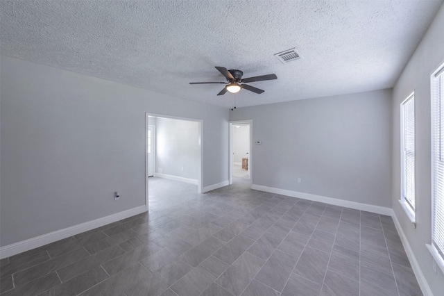 unfurnished room with a textured ceiling, visible vents, a ceiling fan, and baseboards