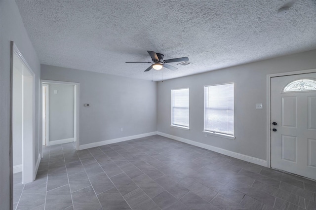 entryway with visible vents, a ceiling fan, dark tile patterned floors, baseboards, and a textured ceiling