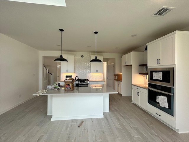 924 Wormwood Dr, League City, TX 77573 - kitchen featuring oven, stainless steel microwave, light wood-style floors, backsplash, and white cabinetry