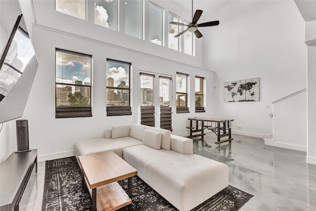 living room with a towering ceiling, finished concrete flooring, baseboards, and ceiling fan