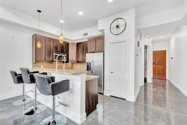 kitchen featuring visible vents, a peninsula, a breakfast bar, light stone countertops, and stainless steel appliances