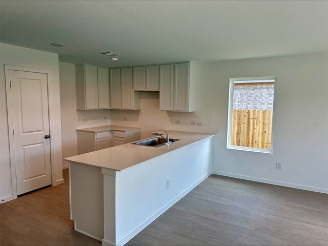 kitchen with dark wood-type flooring, a sink, baseboards, a peninsula, and light countertops