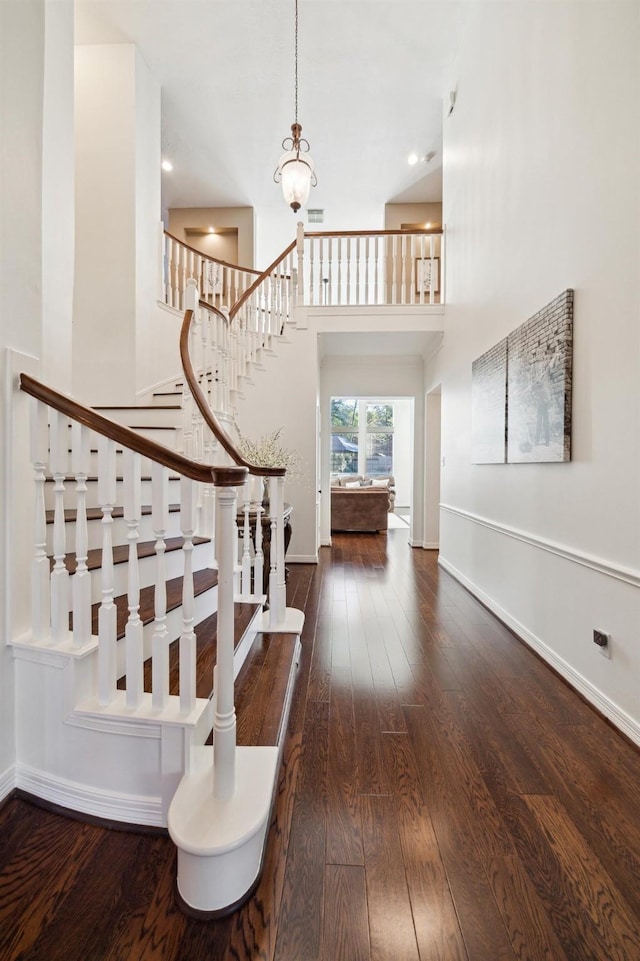 stairway featuring a towering ceiling, wood-type flooring, and baseboards
