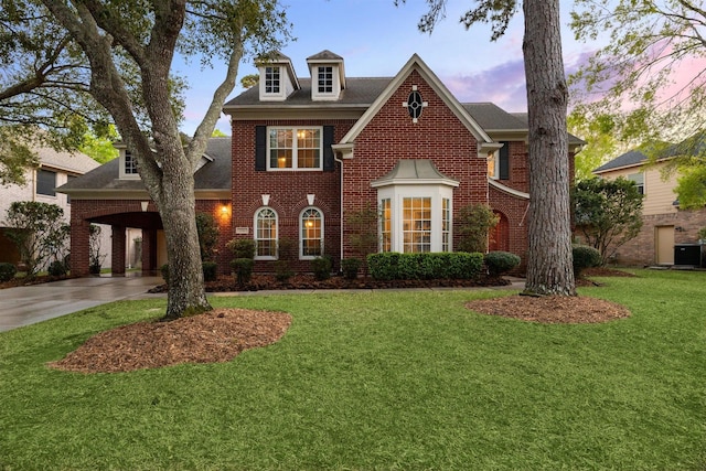 colonial-style house with a yard, brick siding, driveway, and central AC unit