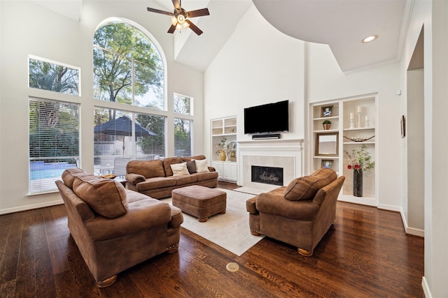living area featuring ceiling fan, built in shelves, baseboards, and a high ceiling
