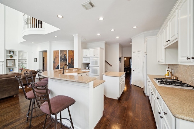 kitchen with a sink, white appliances, visible vents, recessed lighting, and a center island with sink