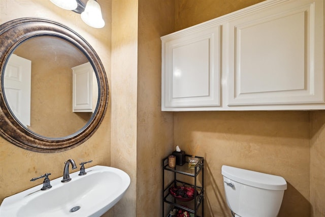 half bathroom with a textured wall, toilet, and a sink