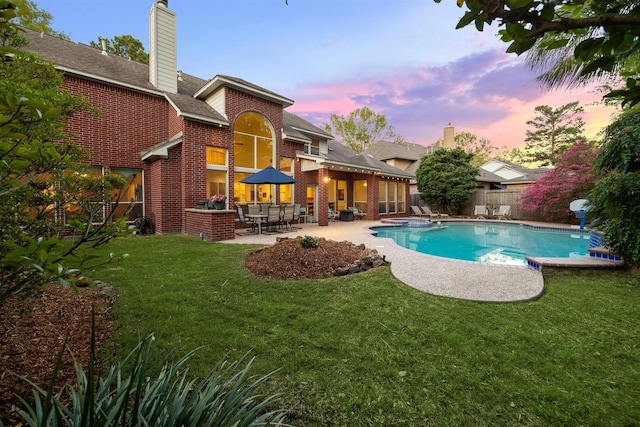 pool at dusk featuring a yard, an outdoor pool, a patio area, and a fenced backyard