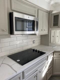 5535 Spellman Rd, Houston, TX 77096 - kitchen featuring light stone counters, tasteful backsplash, crown molding, black electric stovetop, and stainless steel microwave