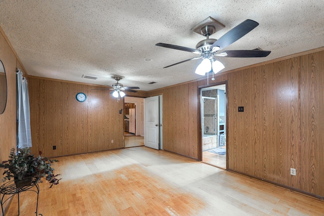empty room with wood finished floors, a ceiling fan, a textured ceiling, wood walls, and visible vents