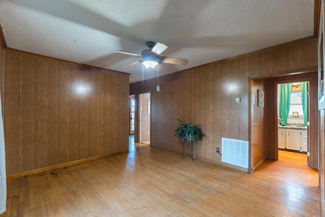 empty room with ceiling fan, wood walls, light wood finished floors, and visible vents