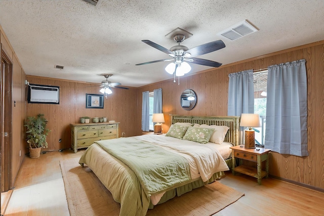 bedroom featuring light wood finished floors, wooden walls, a textured ceiling, and visible vents