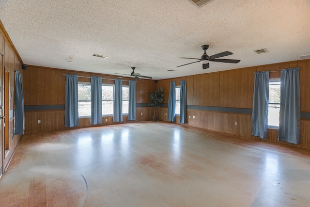 unfurnished room with wooden walls, healthy amount of natural light, a textured ceiling, a ceiling fan, and light wood-type flooring