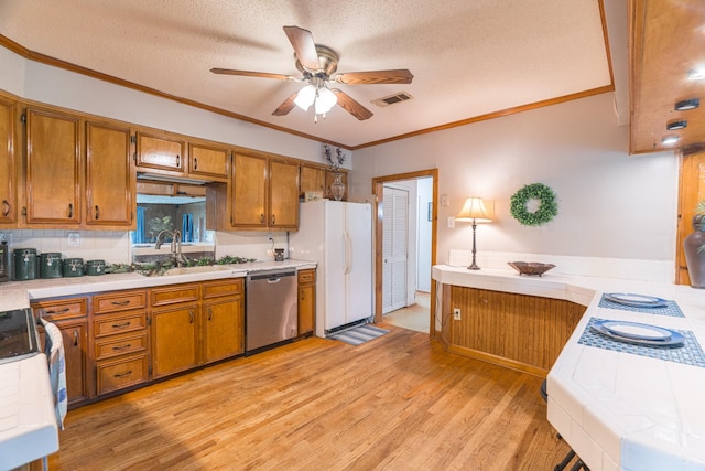 kitchen with a sink, brown cabinets, freestanding refrigerator, tile countertops, and dishwasher