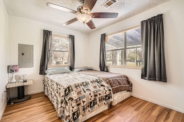 bedroom featuring a textured ceiling, visible vents, electric panel, and wood finished floors