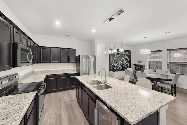 kitchen featuring a sink, appliances with stainless steel finishes, a center island with sink, beverage cooler, and visible vents