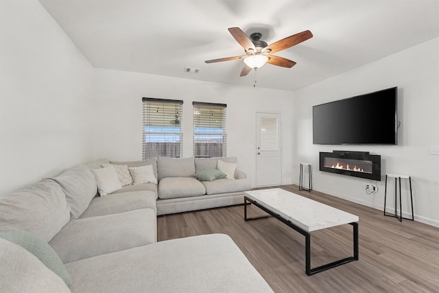 living area with baseboards, visible vents, a ceiling fan, a glass covered fireplace, and wood finished floors