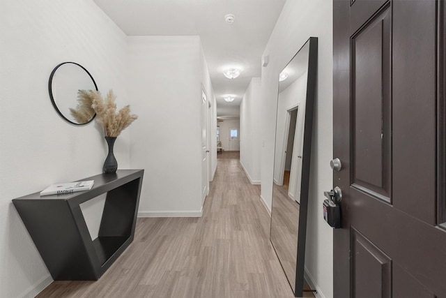 corridor featuring light wood finished floors and baseboards