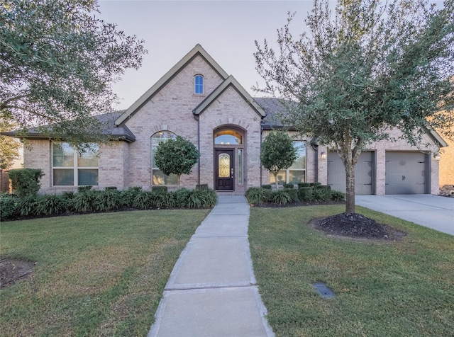french country inspired facade featuring a front lawn, a garage, brick siding, and concrete driveway