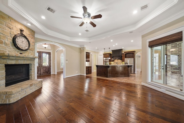 33922 High Point Dr, Magnolia, TX 77355 - unfurnished living room with arched walkways, a tray ceiling, a stone fireplace, a ceiling fan, and ornamental molding
