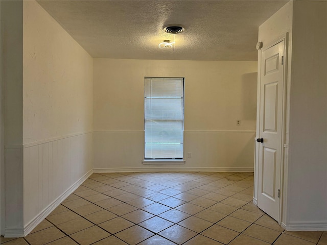 spare room featuring light tile patterned flooring, a textured ceiling, visible vents, and wainscoting