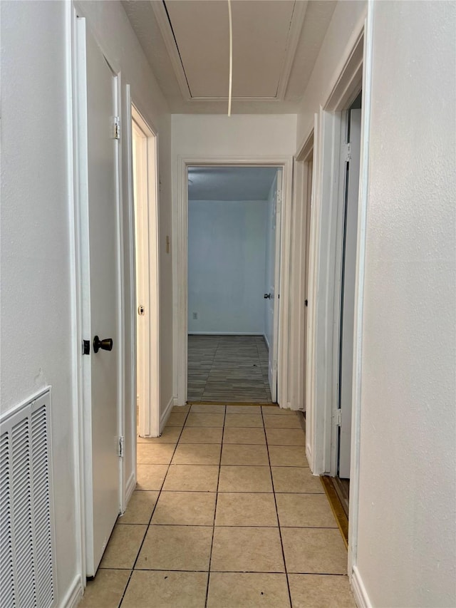 hall with attic access, light tile patterned flooring, and visible vents