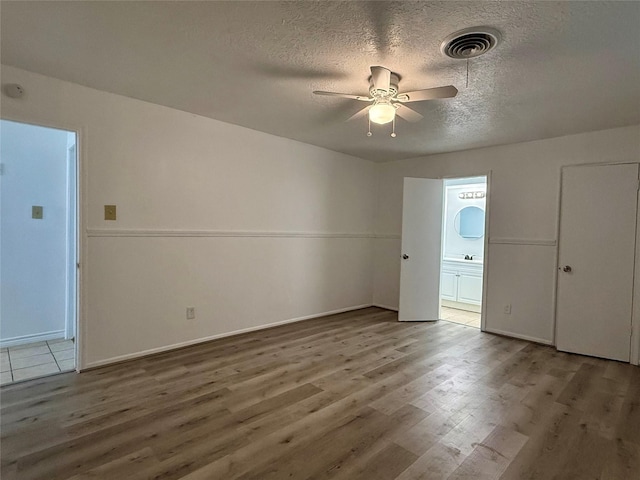 interior space with a ceiling fan, wood finished floors, visible vents, and a textured ceiling