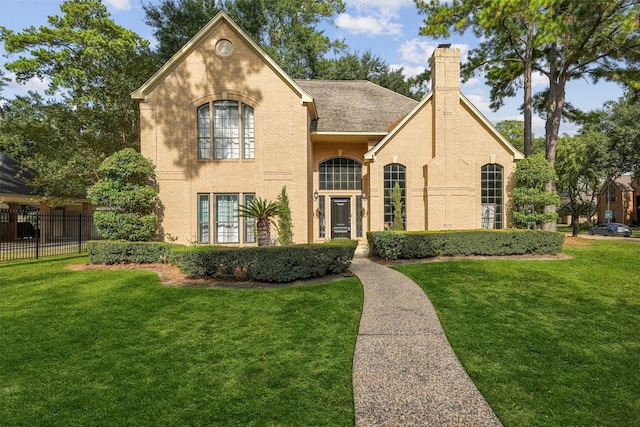 view of front of home with brick siding, a chimney, fence, and a front lawn