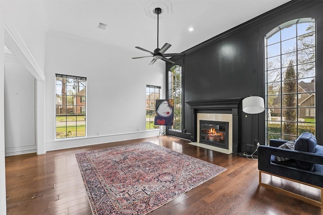 living area featuring crown molding, ceiling fan, a fireplace with flush hearth, visible vents, and hardwood / wood-style flooring