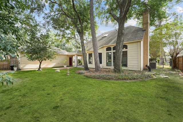 rear view of property featuring roof with shingles, a chimney, fence, and a lawn