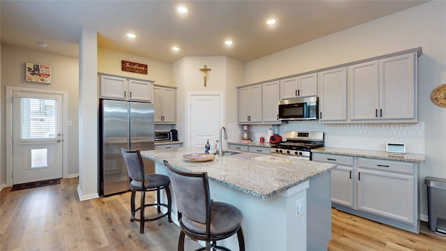 21586 Jordan Pond Rdg, Porter, TX 77365 - kitchen with stainless steel appliances, a sink, light stone counters, a kitchen bar, and light wood-style flooring