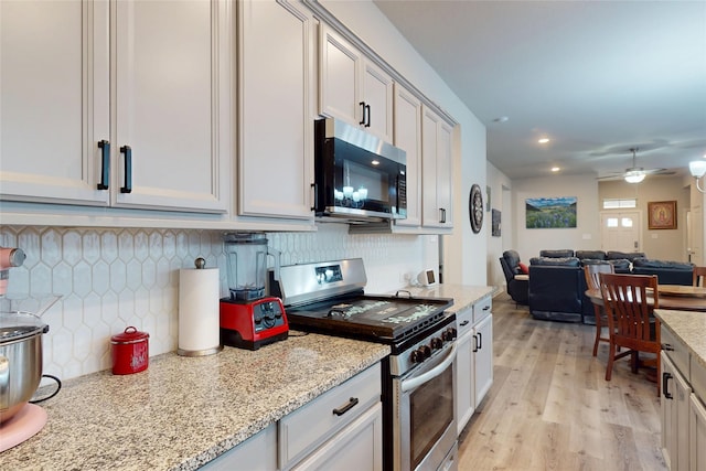21586 Jordan Pond Rdg, Porter, TX 77365 - kitchen featuring stainless steel appliances, open floor plan, light wood-style floors, backsplash, and light stone countertops