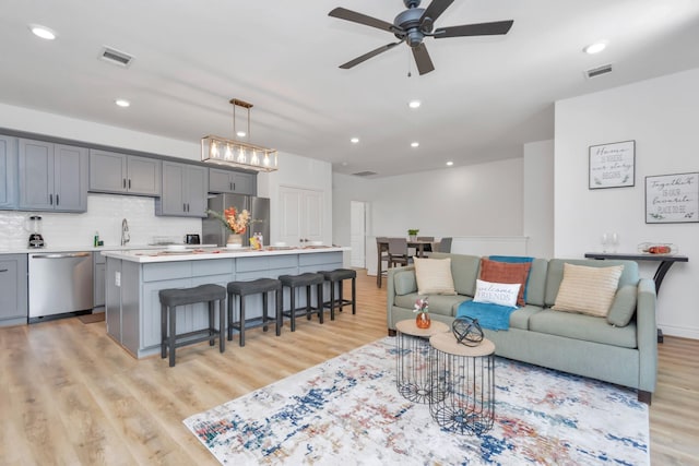 living area with light wood-type flooring, ceiling fan, and visible vents