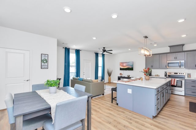 kitchen with light countertops, a kitchen island, appliances with stainless steel finishes, gray cabinetry, and light wood-type flooring