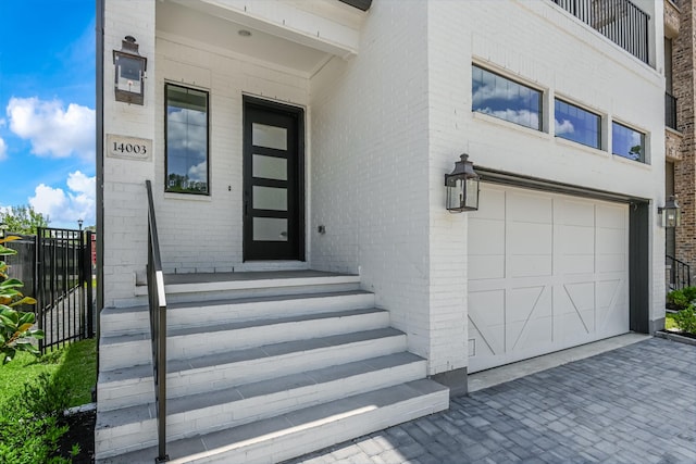 doorway to property featuring brick siding, driveway, fence, and an attached garage