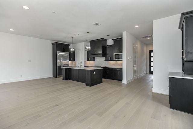 kitchen featuring light countertops, light wood-type flooring, backsplash, appliances with stainless steel finishes, and dark cabinets