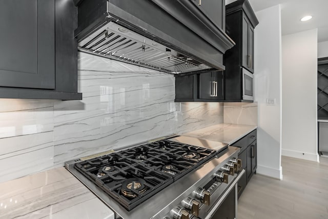 kitchen featuring stainless steel appliances, range hood, decorative backsplash, light wood-style floors, and dark cabinets