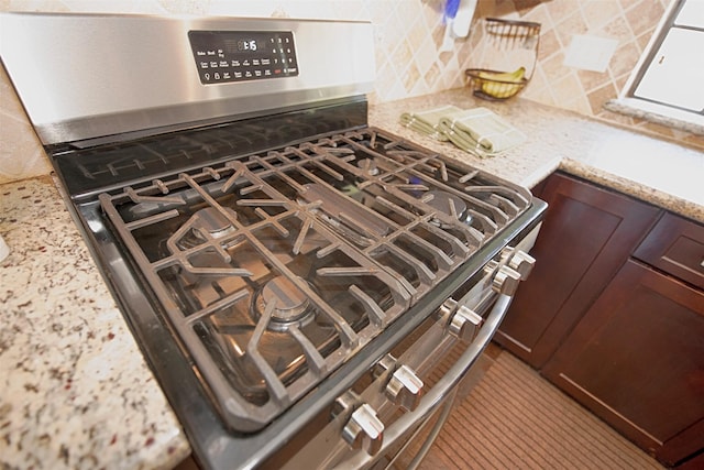 kitchen view of stainless steel gas range oven, decorative backsplash, and light stone counters
