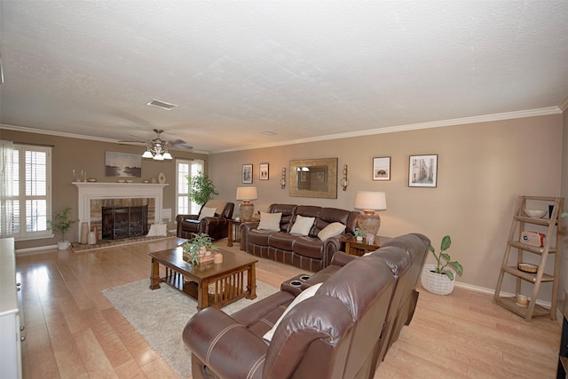 living room featuring ceiling fan, light wood-style flooring, baseboards, a tiled fireplace, and a textured ceiling