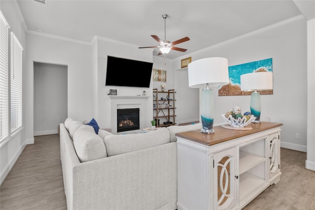 4831 Dove Cove Ln, League City, TX 77573 - living area with light wood-style flooring, crown molding, baseboards, a ceiling fan, and a glass covered fireplace
