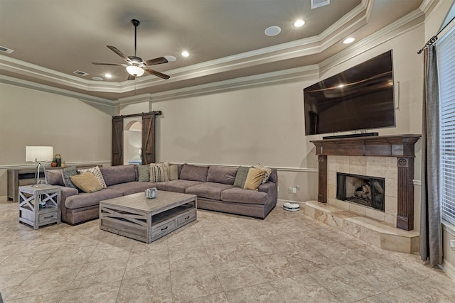 living area featuring visible vents, ceiling fan, ornamental molding, a tiled fireplace, and a raised ceiling