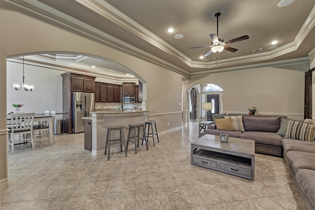 living area featuring baseboards, ornamental molding, a raised ceiling, arched walkways, and ceiling fan with notable chandelier