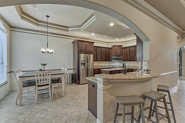 kitchen with a raised ceiling, appliances with stainless steel finishes, arched walkways, decorative backsplash, and dark brown cabinets