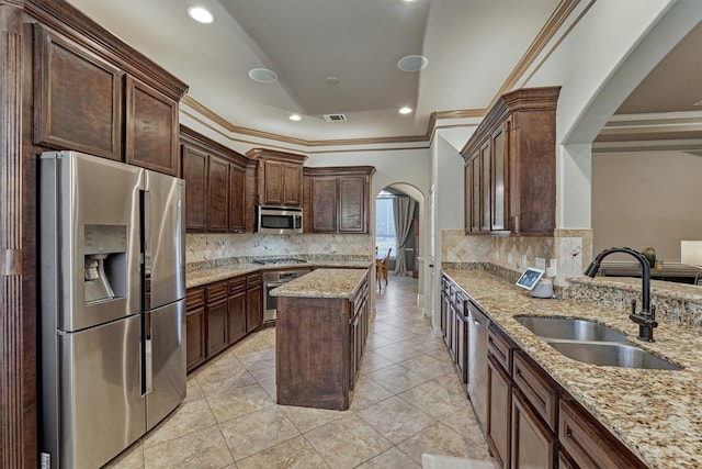 kitchen with light stone counters, a sink, tasteful backsplash, stainless steel appliances, and arched walkways