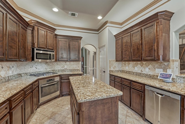 kitchen featuring a kitchen island, light stone countertops, appliances with stainless steel finishes, visible vents, and arched walkways