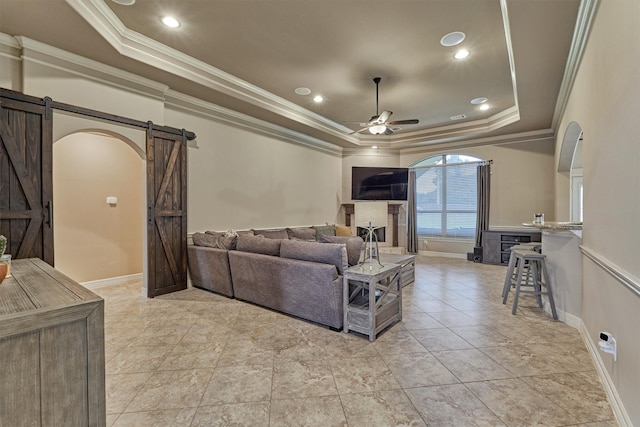 living room featuring a tray ceiling, crown molding, a barn door, baseboards, and ceiling fan
