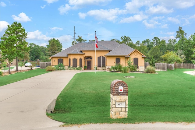 view of front facade with stucco siding, fence, driveway, a front yard, and a shingled roof