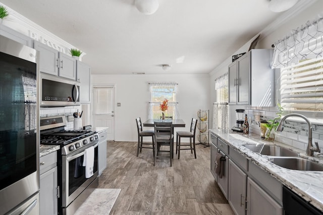 kitchen featuring gray cabinets, backsplash, stainless steel appliances, light wood finished floors, and a sink