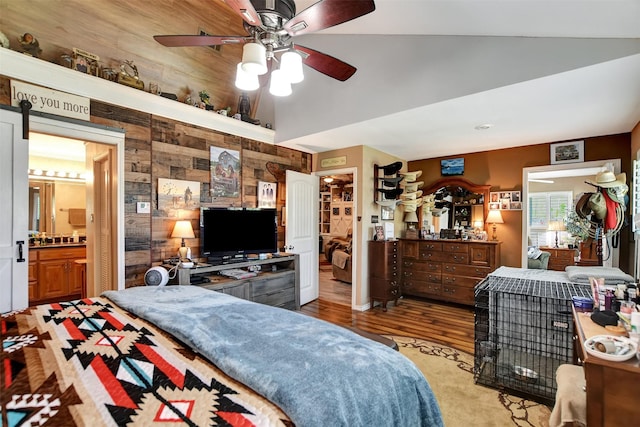 bedroom featuring high vaulted ceiling, wood finished floors, wooden walls, ceiling fan, and ensuite bath